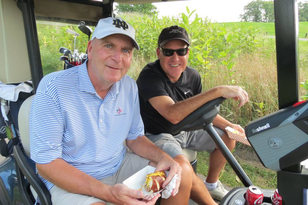 Two men in golf cart with hotdogs